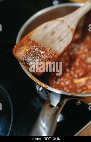 Cuillère en bois remuant la sauce tomate épaisse dans une casserole Banque D'Images