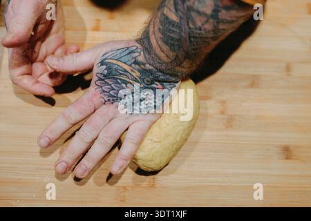 Mains tatouées pressant la pâte fraîche sur une planche de bois Banque D'Images
