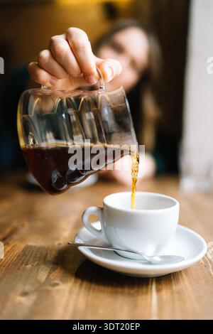 Verser le café noir à la main à partir de la carafe en verre dans une tasse blanche Banque D'Images