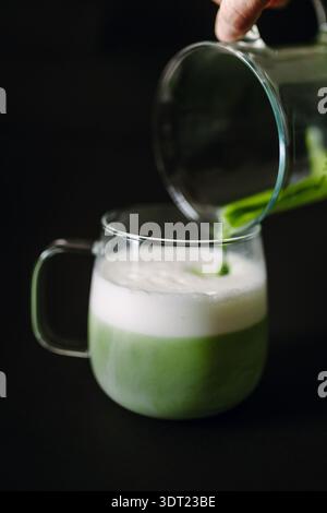 Un moment serein d'un latte matcha versé dans une tasse en verre, montrant la couleur verte vibrante et la mousse blanche mousseuse. Parfait pour une pause détente o Banque D'Images