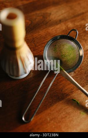 Gros plan des outils de préparation du matcha sur une table en bois. Un fouet en bambou et un tamis métallique sont utilisés pour faire du thé japonais traditionnel, soulignant le v Banque D'Images