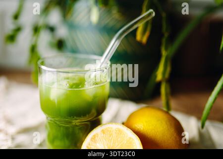 Un verre rafraîchissant de thé matcha glacé avec une paille claire se trouve sur une table à côté de tranches de citron frais, offrant une exper de boisson vibrante et rajeunissante Banque D'Images