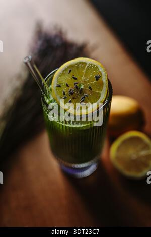 Une boisson matcha vert vif est élégamment servie dans un verre avec une tranche de citron ornée de bourgeons de lavande. Cette boisson rafraîchissante combine terreuse Banque D'Images
