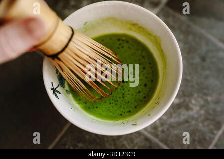 Une vue rapprochée du thé matcha mousseux préparé avec un fouet traditionnel en bambou dans un bol en céramique. Le thé vert éclatant contraste magnifiquement avec l'esprit Banque D'Images
