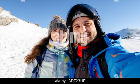 Un couple souriant profite d'une journée ensoleillée de ski à Puerto de Navacerrada, Madrid. Vêtus de vêtements d'hiver, ils capturent la joie d'une escapade hivernale parfaite Banque D'Images