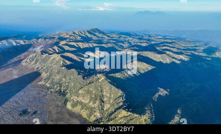 Le vaste étage de la caldeira rencontre le Mont bromo fumant et le lointain Semeru, où les pentes de cendres, le brouillard et les pics volcaniques s'alignent sous un ciel bleu impeccable. Banque D'Images