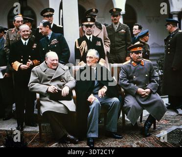 Cette photographie emblématique de 1945 capture les « trois grands » leaders lors de la conférence de Yalta en février 1945. De gauche à droite, Winston Churchill, Franklin D. Roosevelt et Joseph Staline, accompagnés de divers militaires et diplomates, discutent de la réorganisation de l'Europe après la seconde Guerre mondiale. Cette rencontre historique a joué un rôle crucial dans le façonnement du paysage géopolitique du milieu du XXe siècle. Banque D'Images