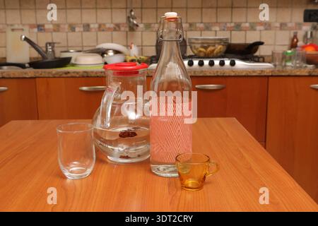 Table de cuisine montrant une carafe en verre, une bouteille et deux verres vides prêts à servir de l'eau Banque D'Images