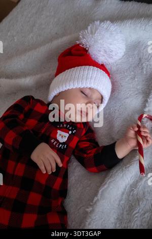Bébé endormi dans le chapeau de père noël tenant la canne de bonbons Banque D'Images