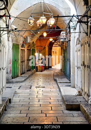 Une rue pavée dans la vieille ville de Jérusalem mène à des magasins et à un vendeur. Les gens se promènent dans le quartier historique, entouré de murs de pierre. Banque D'Images