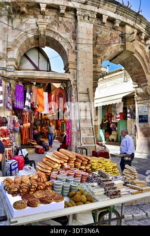 Un étal propose du pain et des bonbons dans la vieille ville de Jérusalem. Les gens marchent à proximité et interagissent avec la scène du marché. Banque D'Images