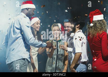 Célébration avec des amis lors d'un rassemblement pendant la saison des fêtes avec boissons et confettis Banque D'Images