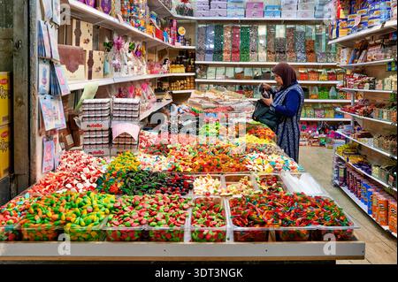 Une femme achète des bonbons colorés et des collations dans une épicerie très fréquentée de la vieille ville de Jérusalem. De nombreux bonbons et produits sont exposés sur les étagères. Banque D'Images