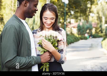 Couple partage un moment joyeux dans le parc avec bouquet de fleurs pendant Sunny Day Banque D'Images