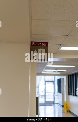 Plan vertical d'un panneau d'ascenseur accroché à un mur blanc dans un couloir public. Le panneau comporte une icône humaine et un symbole d'ascenseur. Dans le backgro Banque D'Images