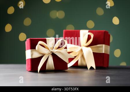 Belles boîtes cadeaux en velours sur une table en bois noir sur fond vert foncé avec des lumières floues, gros plan. Effet bokeh Banque D'Images