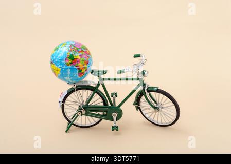 Biciycle de jouet vert vintage avec globe terrestre sur un fond beige. Concept de journée mondiale du vélo et journée sans voiture. Banque D'Images