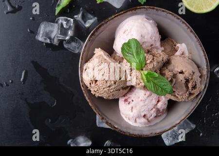 Différentes saveurs de crème glacée servies dans un bol sur une surface sombre avec des feuilles de menthe et du citron vert Banque D'Images