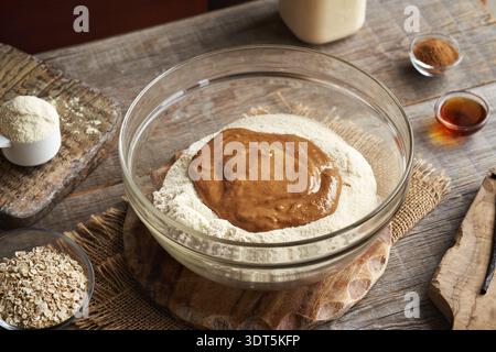 Beurre d'arachide, poudre de protéines de lactosérum et flocons d'avoine moulus dans un bol en verre - préparation de collations saines faites maison Banque D'Images