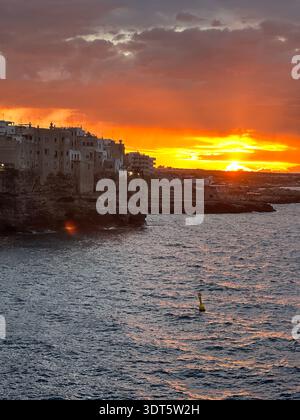 Golden Hour - spectaculaire coucher de soleil orange sur une ville côtière et un rivage rocheux avec des nuages incandescents au-dessus de la mer. Banque D'Images