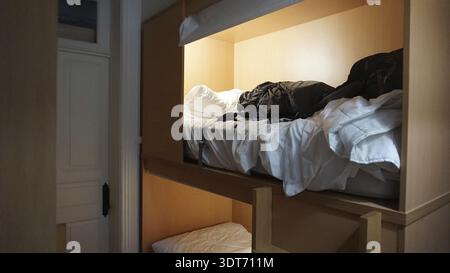 Un lit superposé dans une chambre d'auberge avec des lits et des vêtements non faits, Porto, Portugal Banque D'Images