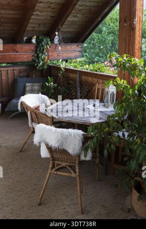Un balcon en bois confortable décoré avec des chaises en osier, des coussins moelleux et des plantes vertes luxuriantes, créant un coin naturel relaxant rempli de lumière du soleil et Banque D'Images