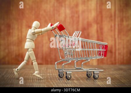 Client avec panier. Allons faire du shopping ! Mannequin en bois poussant un chariot vide Banque D'Images