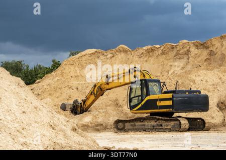Pelle hydraulique jaune pendant le terrassement à une fosse ouverte sur fond ciel bleu foncé. Machines de construction et équipements lourds de terrassement pour l'excavation, l Banque D'Images