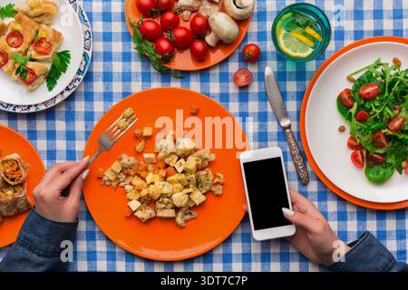 Manger un repas avec des assiettes colorées et un smartphone sur la table pendant le déjeuner Banque D'Images