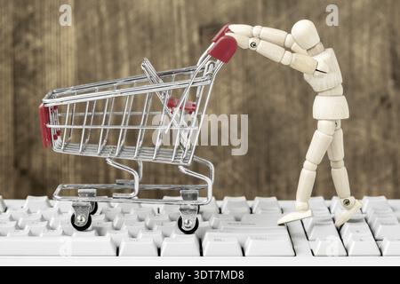 Mannequin en bois poussant le chariot vide sur le clavier de l'ordinateur. Concept d'achat en ligne. E-commerce Banque D'Images