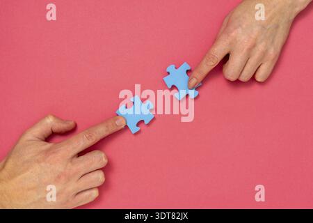 Mains de femme et d'homme pièces de puzzle bleu sur fond rose. Concept de relation Banque D'Images