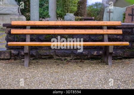 Banc en bois vide dans un cimetière avec des pierres tombales en arrière-plan, symbolisant le deuil, le souvenir, le chagrin, la perte, réflexion et mémoire paisible. Banque D'Images