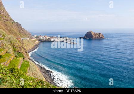 Côte de Porto Moniz. Le promontoire rocheux et le petit port se trouvent à côté des eaux bleues profondes de l'Atlantique. L'îlot volcanique s'élève au large près du rivage de roches de lave. Banque D'Images