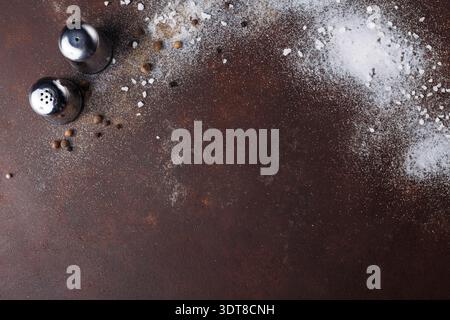 Salière et poivrière sur une surface brune avec épices éparpillées et sel Banque D'Images