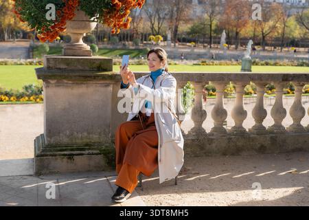 Femme souriante prenant selfie smartphone dans le jardin européen ensoleillé d'automne Banque D'Images