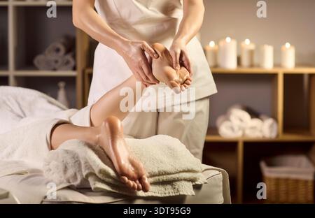 Gros plan massage des pieds dans le salon de spa, masseur mains relaxant client par des bougies Banque D'Images