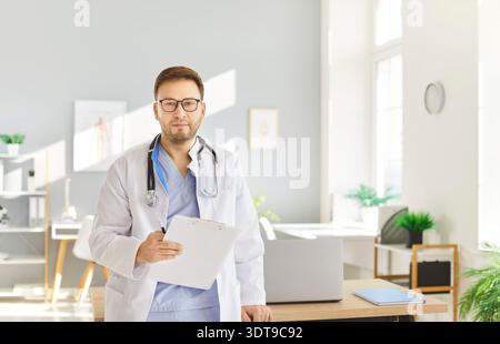 Portrait professionnel d'un médecin masculin souriant portant un uniforme médical blanc, stéthoscope et lunettes Banque D'Images