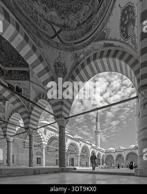 Edirne, Turquie – mai 2022 : vue en noir et blanc d’un homme debout dans la cour historique de la mosquée UC Serefeli sous des arches rayées. Banque D'Images