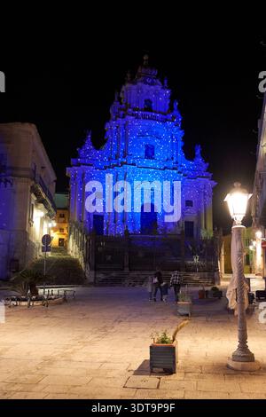 Les gens marchent près du Duomo de San Giorgio à Modica. La cathédrale est éclairée par des lumières bleues pendant la nuit. Banque D'Images