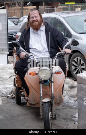 Portrait posé d'un homme juif hassidique avec les cheveux roux et la barbe assis sur un scooter de livraison à 3 roues. À New York, hiver 2026. Banque D'Images