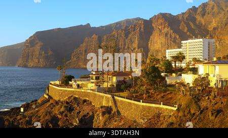 Falaises côtières ensoleillées s'élevant au-dessus de l'Atlantique sur Tenerife, avec des stations balnéaires et des terrasses bordées de palmiers surplombant l'océan calme, capturant l'EI Banque D'Images