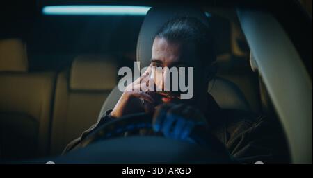 Jeune conducteur masculin se dispute intensément au téléphone assis à l'intérieur de la voiture. Young Man Raisses Voice, clairement engagé dans une discussion animée avec quelqu'un de proche. Concept de conflit relationnel et stress personnel. Banque D'Images