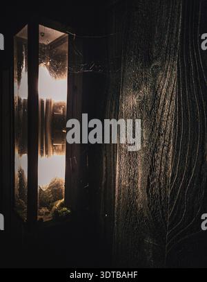 Gros plan d'une lanterne projetant une lueur chaude sur un mur de bois sombre. La lumière met en valeur les textures complexes du bois, tandis que les toiles d'araignée s'étirent Banque D'Images