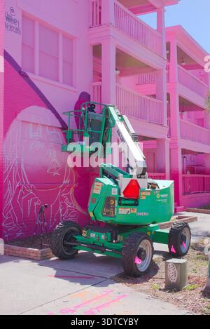 Ouvrier peignant la peinture murale du bâtiment rose brillant de Green Boom Lift sur Sunny Street. Usage éditorial seulement 20 février 2026 produit Petersburg, FL USA. Travailleur sur un g. Banque D'Images