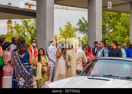 Arkansas, 10 août 2024 - mariée indienne et mariée en tenue traditionnelle sortent d'une voiture blanche que les invités se rassemblent sous la structure moderne en béton pour le CER de mariage Banque D'Images