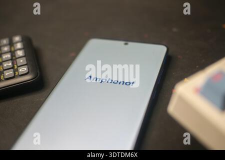 Téléphone affichant le logo Amphenol près d'une calculatrice sur un bureau Banque D'Images