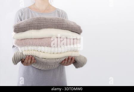 Pile de pulls confortables ou des couvertures couleurs tendance pastel en mains d'une jeune femme contre le mur Banque D'Images