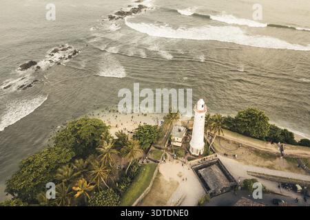 Vue aérienne de haut en bas des Sri Lankais profitant d'une baignade dans l'océan près de l'emblématique phare blanc de Galle Fort. La scène mêle architectural historique Banque D'Images