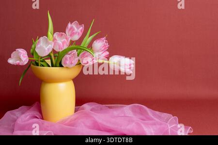 Élégant motif floral pastel orné de tulipes rose blush dans un vase en céramique jaune sur un châle rose doux. Esthétique romantique sophistiquée avec Banque D'Images