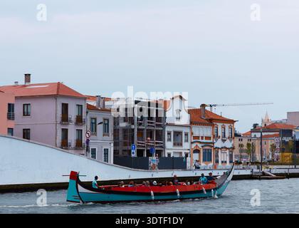 Aveiro, Portugal - 14 juin 2025 : bateau coloré traditionnel navigue dans l'eau le long des bâtiments riverains à Aveiro, Portugal sous un ciel nuageux Banque D'Images